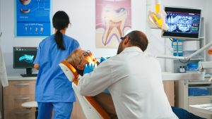 Dentist working in dental unit with nurse and man lying patient
